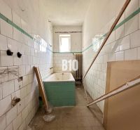 Koupelna rodinného domu s opotřebovanými dlaždicemi a vanou čekající na renovaci.