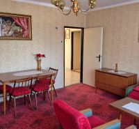 Obývací pokoj s květinovou dekorací v rodinném domě, červená křesla, vzorovaný koberec.