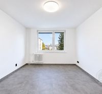 Prostorná místnost s oknem, radiátorem a podlahou s dřevěným dekorem ve 2pokojovém bytě.