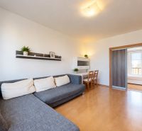 Obývací pokoj v 3-pokojovém bytě s rohovou sedačkou a posuvnými dveřmi.
