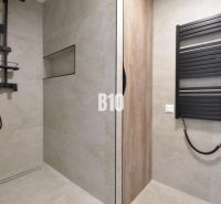 Koupelna ve 4-pokojovém bytě s moderní sprchou a černým radiátorem.