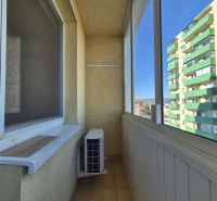 Zasklený balkon v garsonce s klimatizací a výhledem na bytovky.