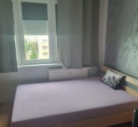 Ložnice v třípokojovém bytě s postelí a šedým dekorativním polštářem.