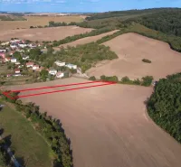 Letecký pohled na zemědělské a lesní pozemky u Podhájské obklopené obcí a lesem.