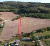 Venkovský výhled na zemědělské a lesní pozemky v Podhájské obklopující osídlení s rodinnými domy.