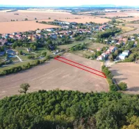 Letecký pohled na zemědělské a lesní pozemky v Podhájské, s vesnicí v pozadí.