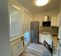 Kuchyně v 2pokojovém bytě s podlahou s dřevěným dekorem, bílými skříňkami a vestavěným spotřebičem.