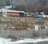 Sněhem pokrytý pozemek s rodinným domem v Oščadnici obklopený zelení a dřevěnými strukturami.