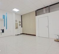 Interiér obchodních prostor s křeslem, zrcadly a dlažbou s bílým vzorem.