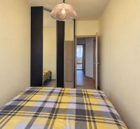 Ložnice s vestavěnou skříní a kostkovaným přehozem ve 3pokojovém bytě.