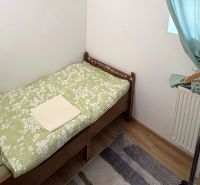 Jednolůžková postel, stojan na oblečení, zelené závěsy, podlaha s dřevěným dekorem.