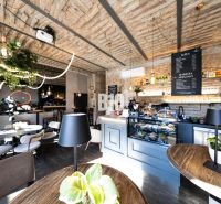 Stylové gastro prostory s cihlovými klenbami, zelení a podlahou s dřevěným dekorem.