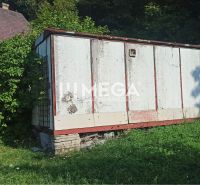 Starší sklad na zahradě ulice v Humenném, obklopený zelení a rostoucí trávou.