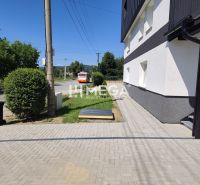Exteriér 4-pokojového bytu v Jasenově s cestou a autobusem, obklopený zelení.