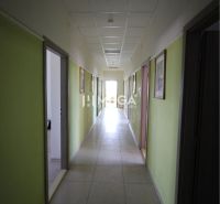 Chodba v kancelářích s bledými stěnami a světlou dlaždicovou podlahou.