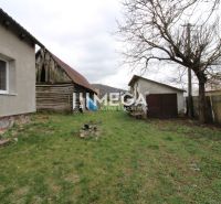 Zahrada u rodinného domu na ulici v Pakostově, se starší dřevěnou kůlnou a trávníkem.