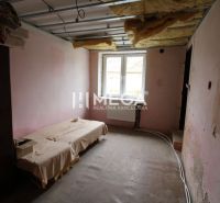 Nezařízený interiér rodinného domu s postelí a odkrytým stropem.