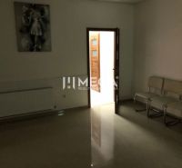 Interiér budovy s bílými židlemi, obrazem a otevřenými dveřmi s nálepkou ověření.