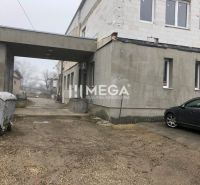 Budova na ulici SNP v Snině se zaparkovaným autem a kontejnerem na štěrkovém povrchu.