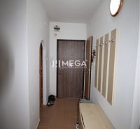 Chodba 2pokojového bytu s věšákovou stěnou, botníkem a hnědými dlaždicemi.