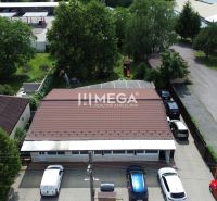 Gastro prostory na Budovatelské ulici ve Vranově nad Topľou obklopené auty a zelení.