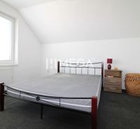 Ložnice v rodinném domě se železnou postelí, nočním stolkem a košem.