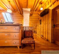 Podkroví rodinného domu se skříní, křeslem a podlahou s dřevěným dekorem.
