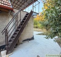 Exteriér chaty v Nových Zámcích s kovovým schodištěm a terasou obklopenou zelení.