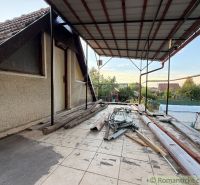 Terasa chaty v Nových Zámcích s nepořádkem a stavebním materiálem, klidná zahrada v pozadí.
