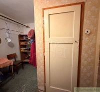 Interiér rodinného domu s předsíní, židlí a regály. Visí tu kuchyňské nástroje.