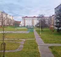 Panelové bytovky obklopují travnatou plochu s chodníky a garsonka.