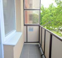 Zasklený balkon s výhledem na zeleň patřící k garsonce.