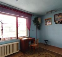 Modrý pokoj s oknem, stolem a židlí v rodinném domě.