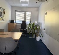 Interiér kanceláře s bílou tabulí, konferenčním stolem a projektorem na stěně budovy.