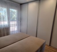 Ložnice v 3-pokojovém bytě s velkou šatní skříní a oknem se záclonami.