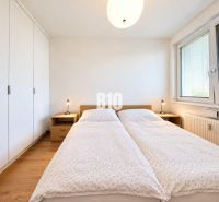 Světlá ložnice s velkou postelí, skříní a podlahou s dřevěným dekorem v 2pokojovém bytě.