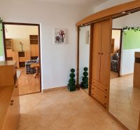 Chodba ve 3-pokojovém bytě s dřevěnými skříněmi a dekoracemi na béžové dlažbě.