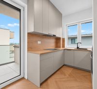 Kuchyně ve 3-pokojovém bytě s podlahou s dřevěným dekorem, výhled na balkon.