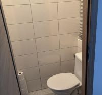 Toaleta s jednoduchým obkladem a dlažbou v 2-pokojovém bytě.