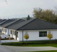 Rodinné domy s tmavou střechou v Hôrce nad Váhom, obklopené zelení a cestou.