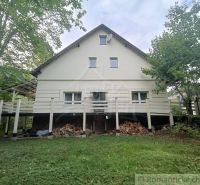 Rodinný dům ve Staškově, obklopený zelení, s dřevem uskladněným pod terasou.