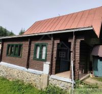 Dřevěná chata s plechovou střechou v přírodě Rajecké Lesné, obklopená zelení.