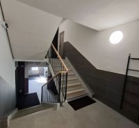 Schodiště bytového domu ve 3-pokojovém bytě s moderními dlaždicemi a zábradlím.