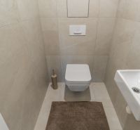 Toaleta se závěsným WC, malým umyvadlem a béžovou dlažbou, Výstavba bytů.