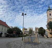 Obchodní prostory v Topoľčanech s dlážděným náměstím a kostelem v pozadí.