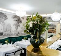 Interiér obchodních prostor se zlatým barem, květinovou dekorací a elegantními stoly.