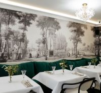 Restaurace s historickou tapetou, křišťálovým lustrem a zelenými sedačkami v obchodních prostorách.