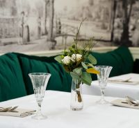 Elegantně prostřený stůl s bílým ubrusem, vázou s květinami a křišťálovými sklenicemi.
