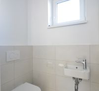 Toaleta s umyvadlem ve 3-pokojovém bytě, jednoduché bílé a šedé barevné schéma.