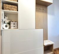 Interiér garsonky s dřevěným nábytkem, dekoracemi a rostlinou na podlaze s dřevěným dekorem.